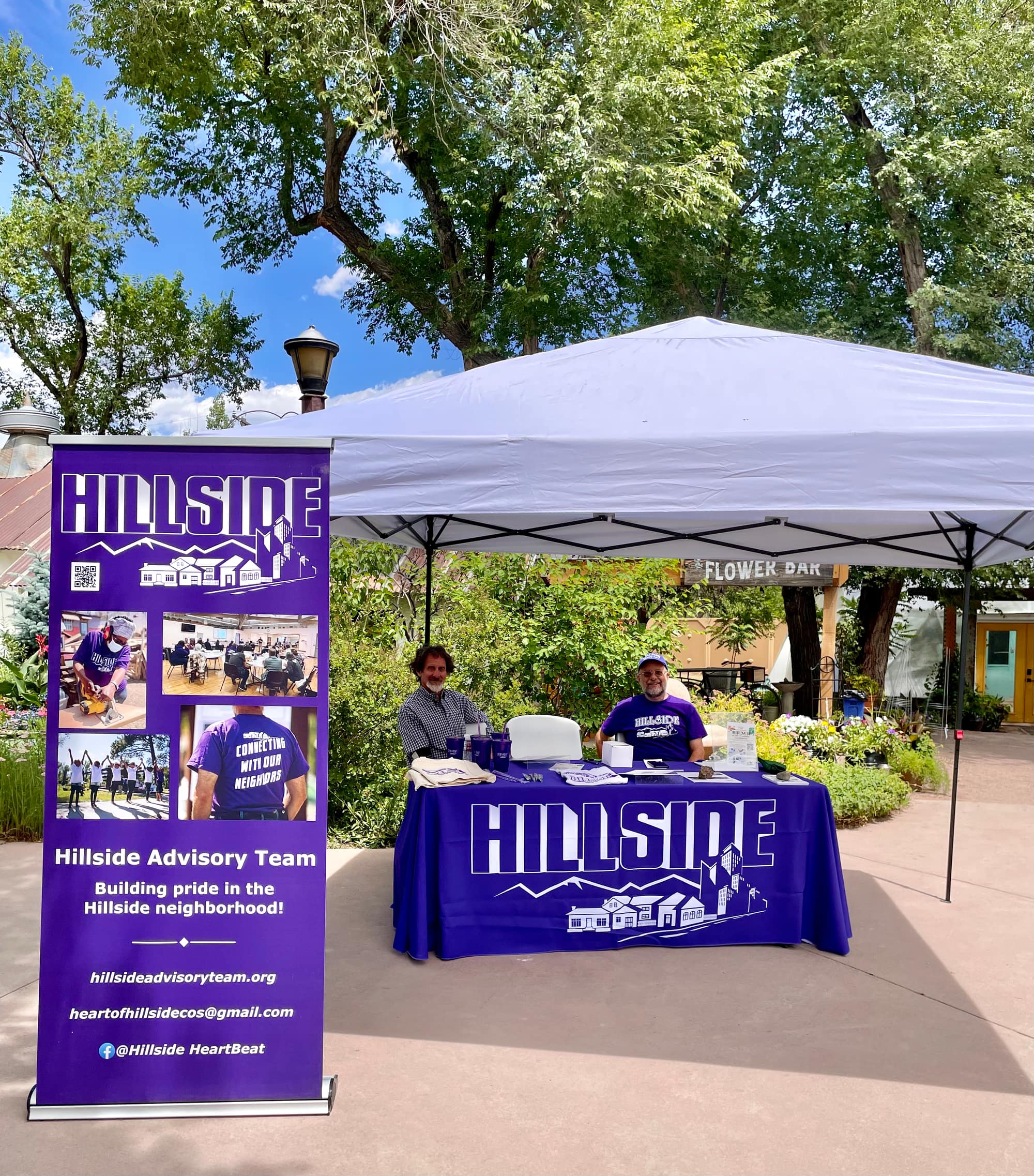 Two volunteers at the Hillside booth, with the purple HILLSIDE banner and tablecloth